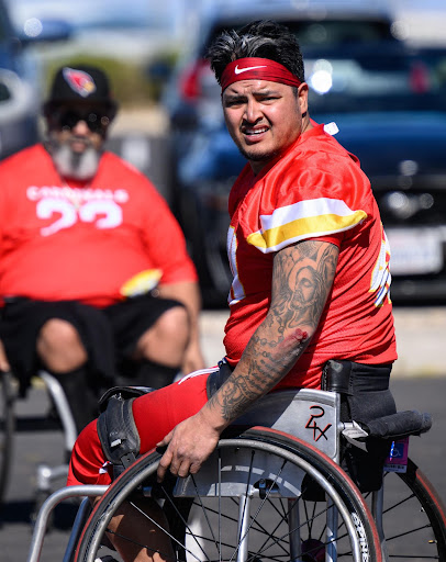 Alex Nguyen, a Kansas City Chiefs wheelchair football player player wearing red jersey with white and gold accents, a sleeve of tattoos on this left arm, and a red Nike headband is seated in wheelchair during the game.