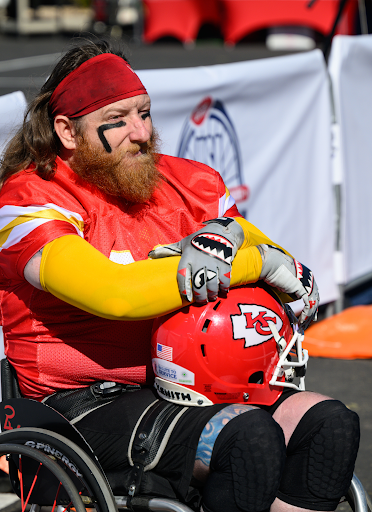 Matthew Scholten, Kansas City Chiefs wearing a red jersey with yellow sleeves and red headband sitting in a wheelchair with the Kansas City Chiefs helmet on his lap.