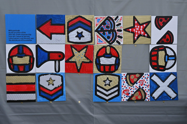 A six- by three-foot mural in red, gold, white, and blue with illustrations of football helmets, arrows, pizzas, badges, and stars